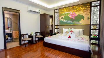 Une chambre d’hôtel avec un grand lit, un plancher en bois, une armoire, un bureau avec une chaise et une salle de bain avec douche et toilettes.