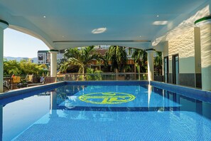 A swimming pool with a circular logo in the center, surrounded by palm trees and a cityscape in the background.