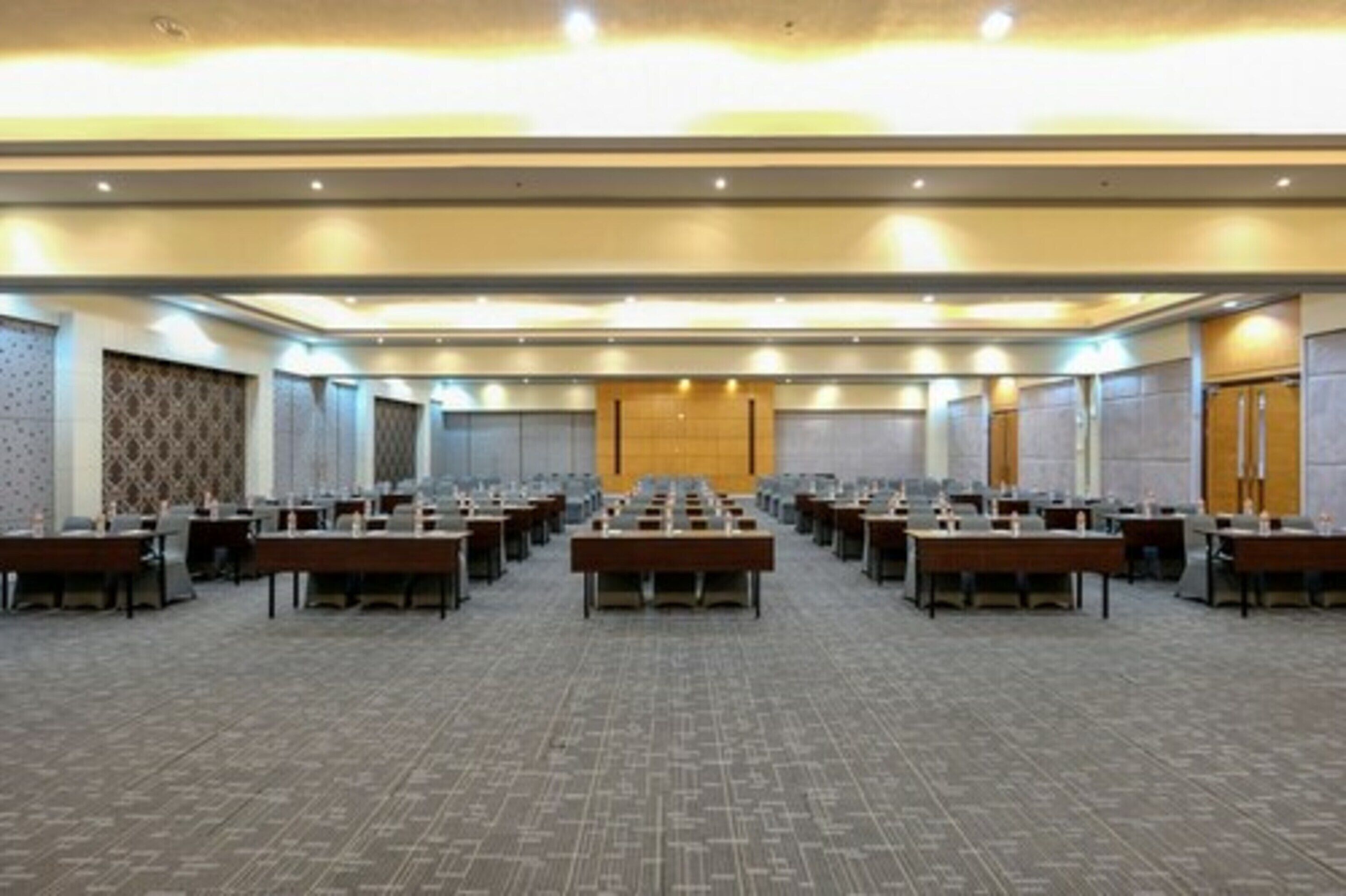 Un salón de conferencias con filas de mesas y sillas, un papel tapiz estampado y una puerta de madera.
