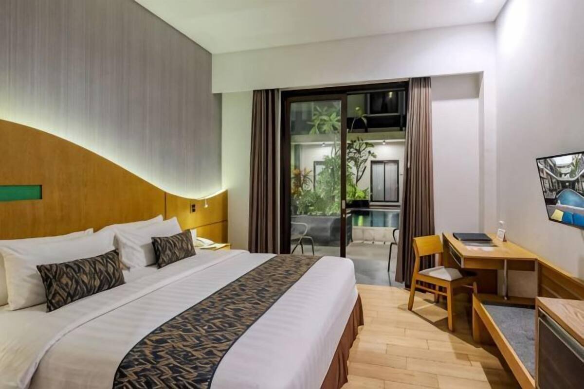 A hotel room with a bed, a desk, a chair, and a view of the outdoors.