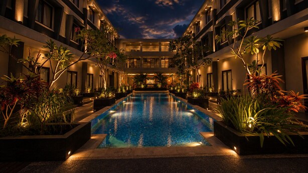 A hotel with a central swimming pool, surrounded by lush greenery and illuminated by warm lighting. - ILLIRA Lite Praya Lombok (Praya)