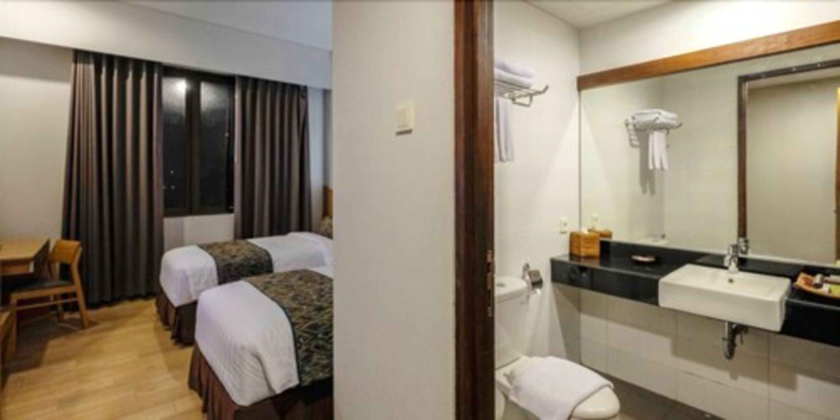 Une chambre d’hôtel avec deux lits, un bureau et une salle de bain équipée d’un lavabo et d’un miroir.