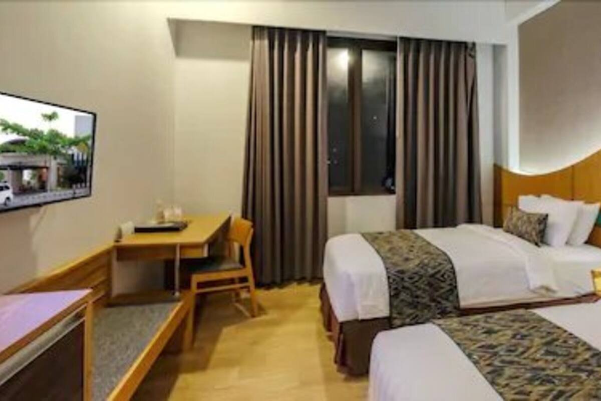 A hotel room with two beds, a desk, a chair, and a TV.