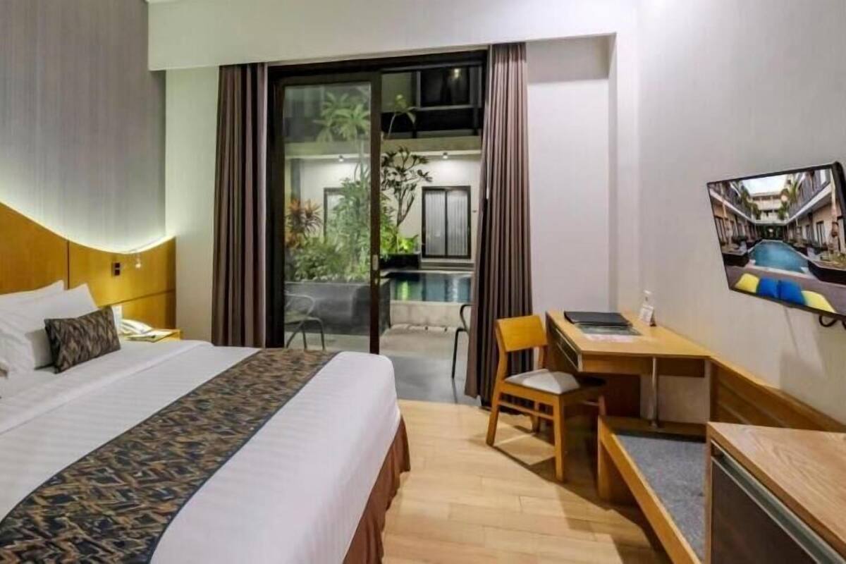 A hotel room with a large bed, a desk, and a view of a pool and outdoor area.