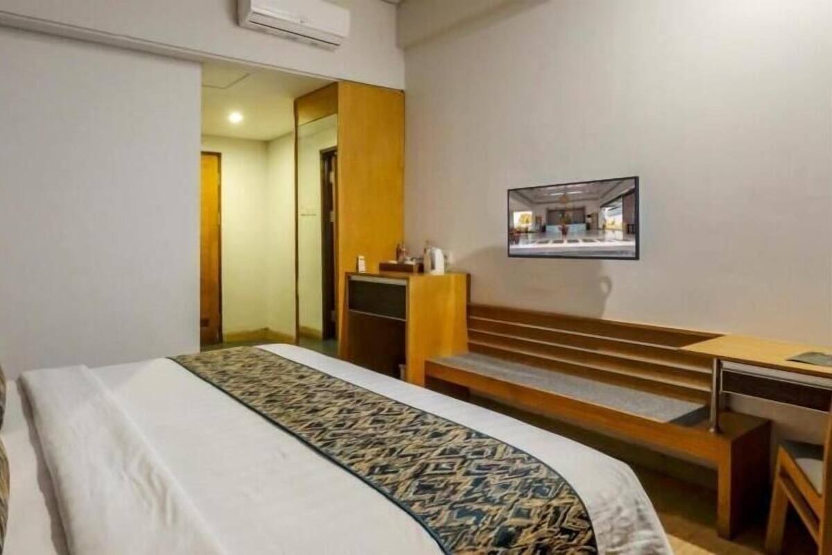 A hotel room with a bed, a desk, a chair, a mirror, and a staircase leading to another room.