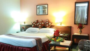 A hotel room with a bed, bedside tables, a nightstand, a chair, and a small table with a vase of flowers. - Hotel Mountain (Kathmandu)