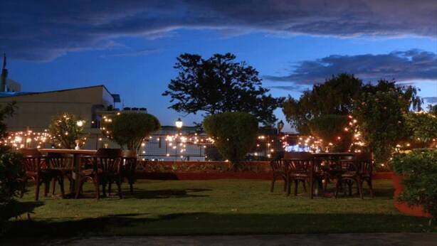 An outdoor dining area with tables and chairs, surrounded by trees and a building in the background. - Hotel Mountain (Kathmandu)