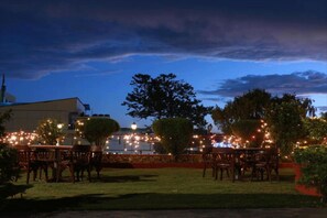 An outdoor dining area with tables and chairs, surrounded by trees and a building in the background. - Hotel Mountain (Kathmandu)