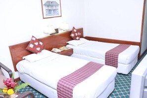 Ein Hotelzimmer mit zwei Einzelbetten, einem Holzkopfstück, Nachttischlampen, einem Telefon, einem gerahmten Bild an der Wand und einem kleinen Tisch mit Blumen.