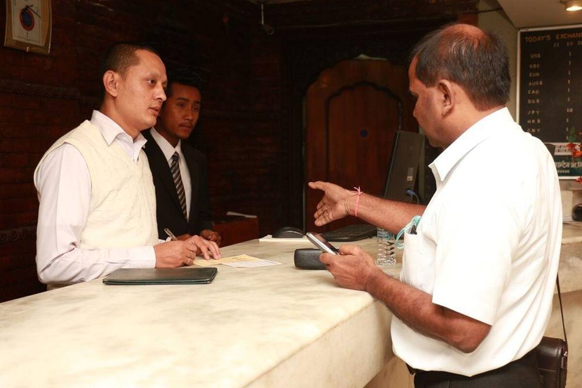 A reception desk with a man in a white shirt and vest, a man in a white shirt, and a man in a suit.