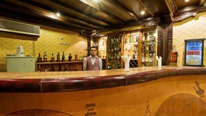 A bar area with wooden bar counter, shelves with bottles, and a person standing behind the counter. - Hotel Mountain (Kathmandu)