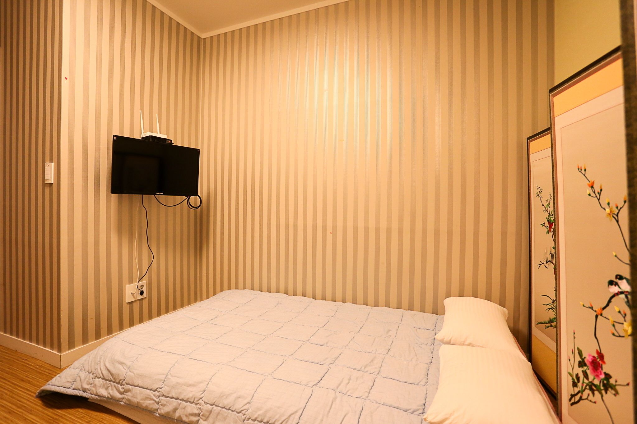 A room with a bed, a mounted television, and a decorative panel with floral artwork.