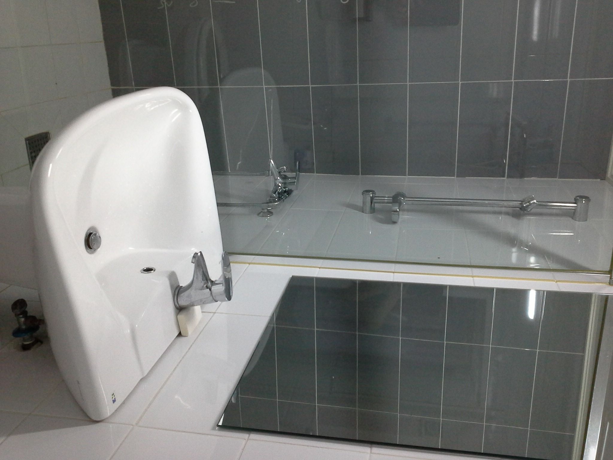 A bathroom with a white pedestal sink, a glass shower enclosure, and a tiled floor.