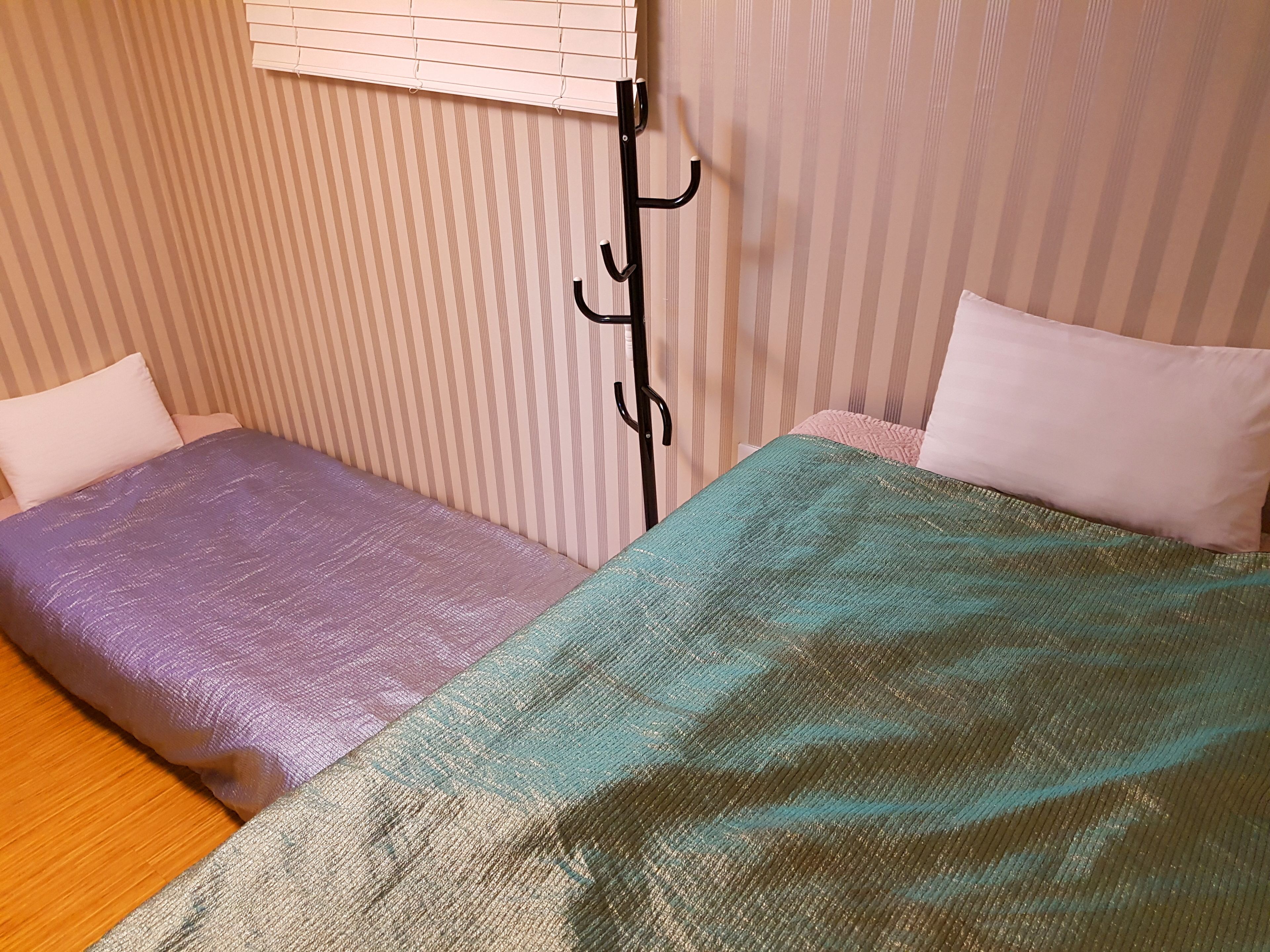 A room with two beds, each with a different colored bedspread. There is a black coat rack with hooks against the wall.