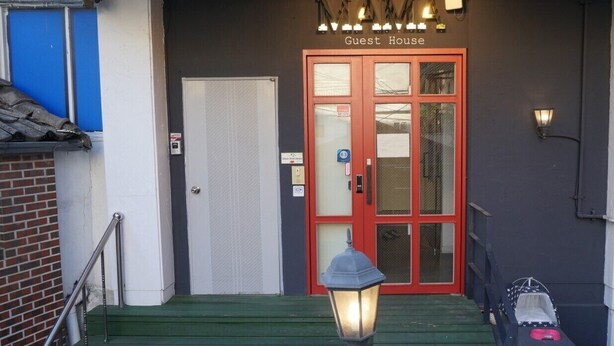 A hotel entrance with a red door, a staircase, and a lamp post.