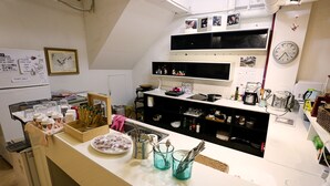 A kitchen with a white countertop, shelves with various kitchen items, a clock, and a refrigerator. - Mama Guest House (Seoul)