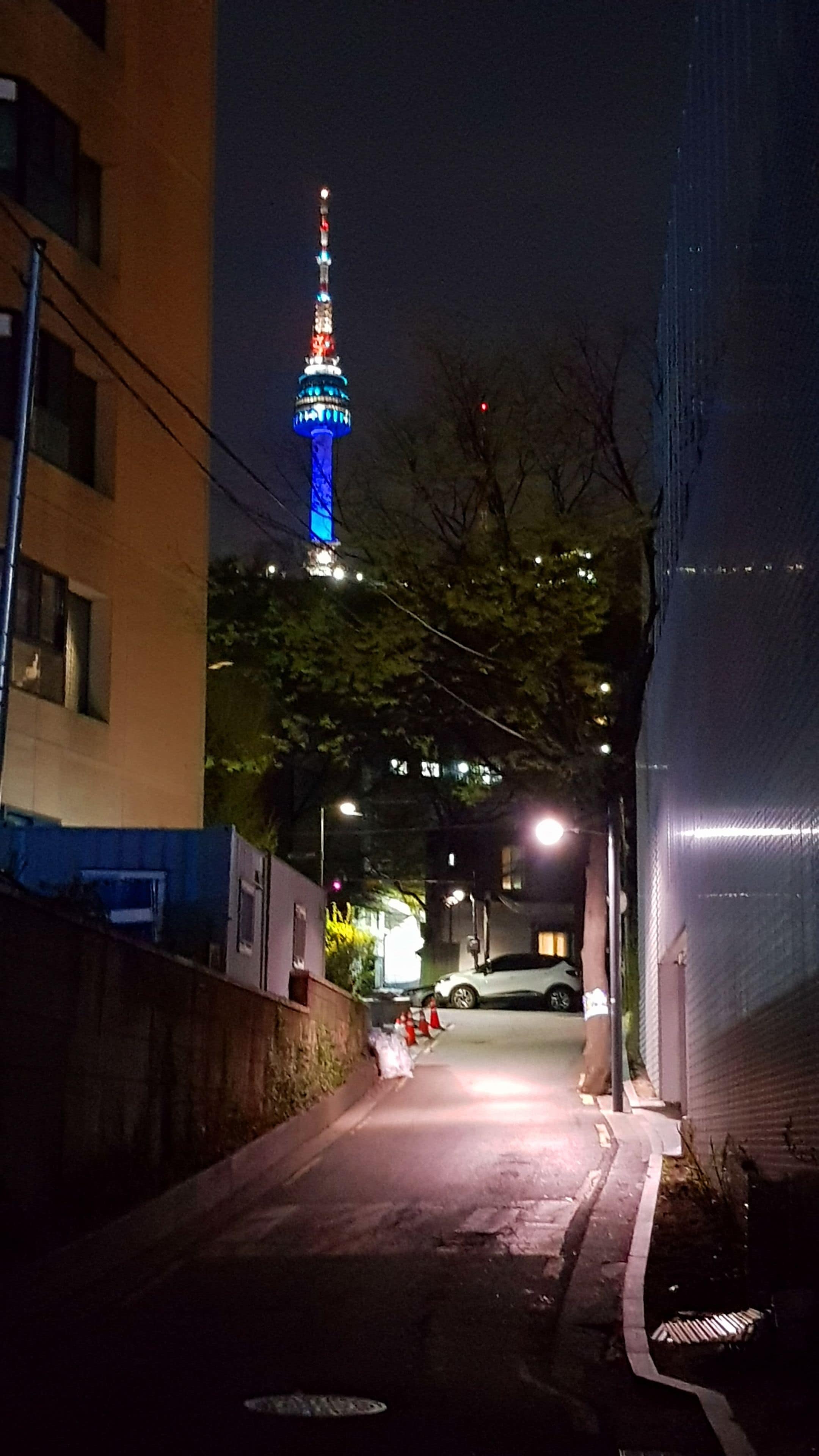 Une vue nocturne d’une rue, avec une tour illuminée qui se détache à l’arrière-plan.