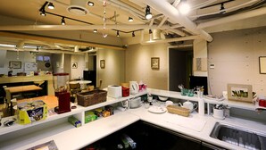 A modern kitchen with white countertops, a built-in stove, and various kitchen appliances. There are shelves with dishes and utensils, and a window providing natural light.