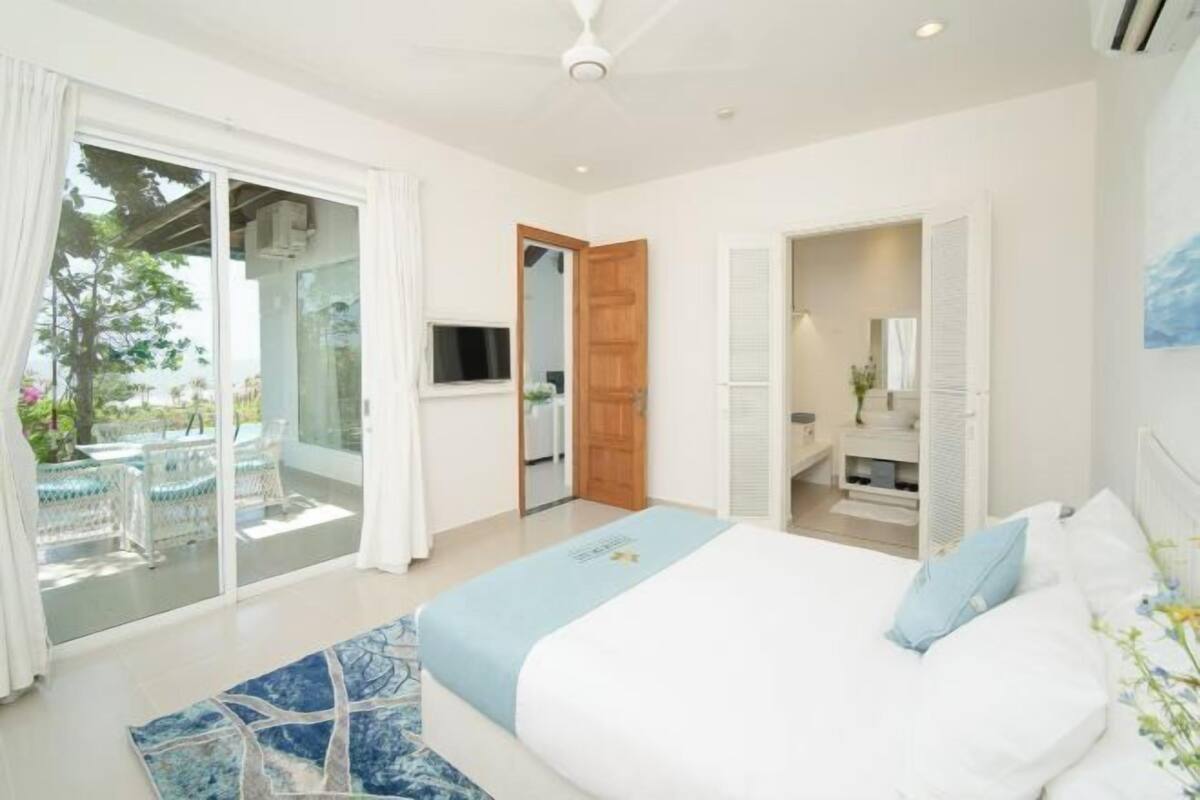 Une chambre à coucher comprenant un lit, une télévision, une salle de bain et une porte-fenêtre coulissante donnant sur un espace extérieur.