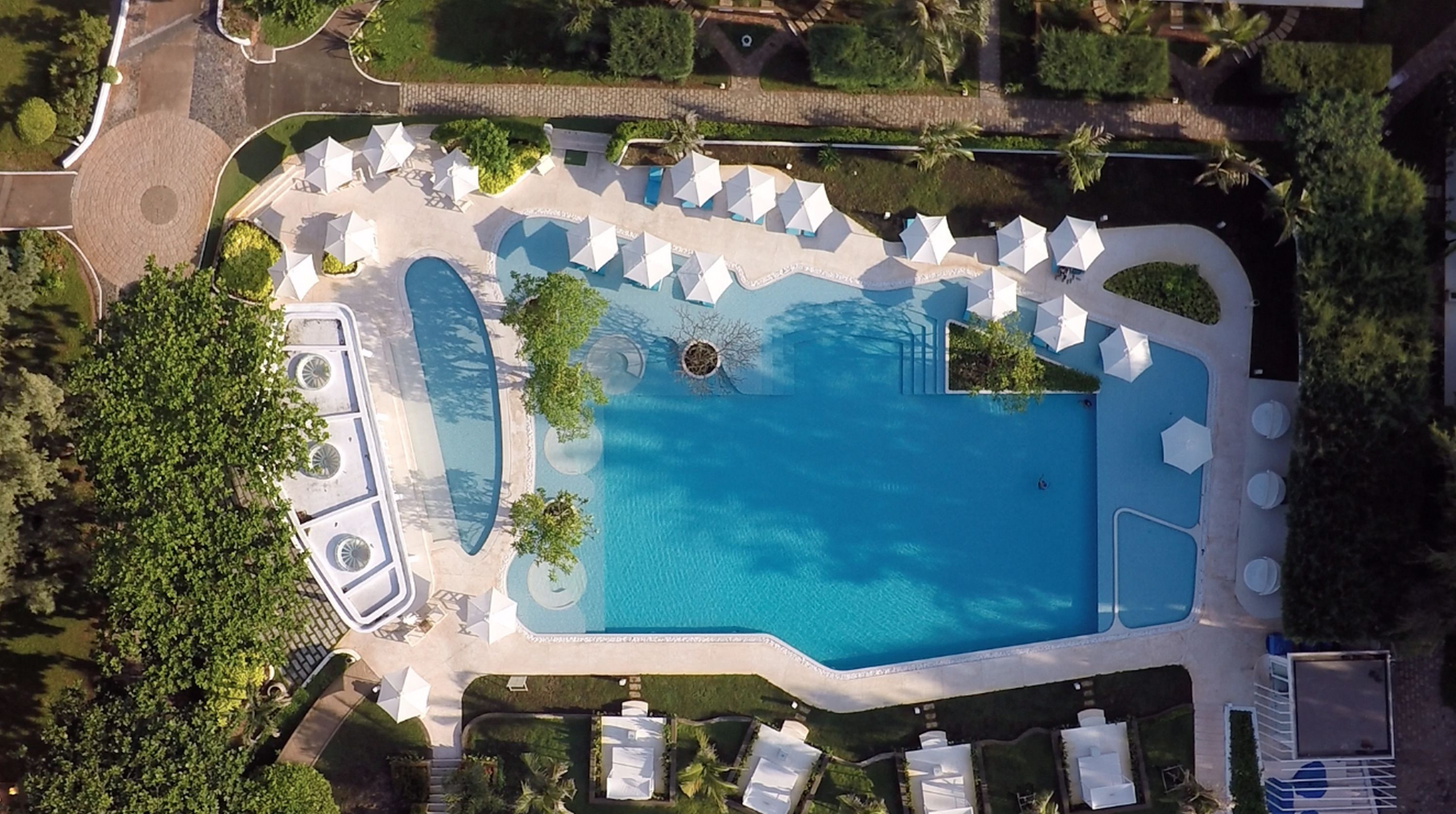 Vue aérienne d’un complexe hôtelier doté d’une grande piscine, de chaises longues et d’un jardin bien entretenu.