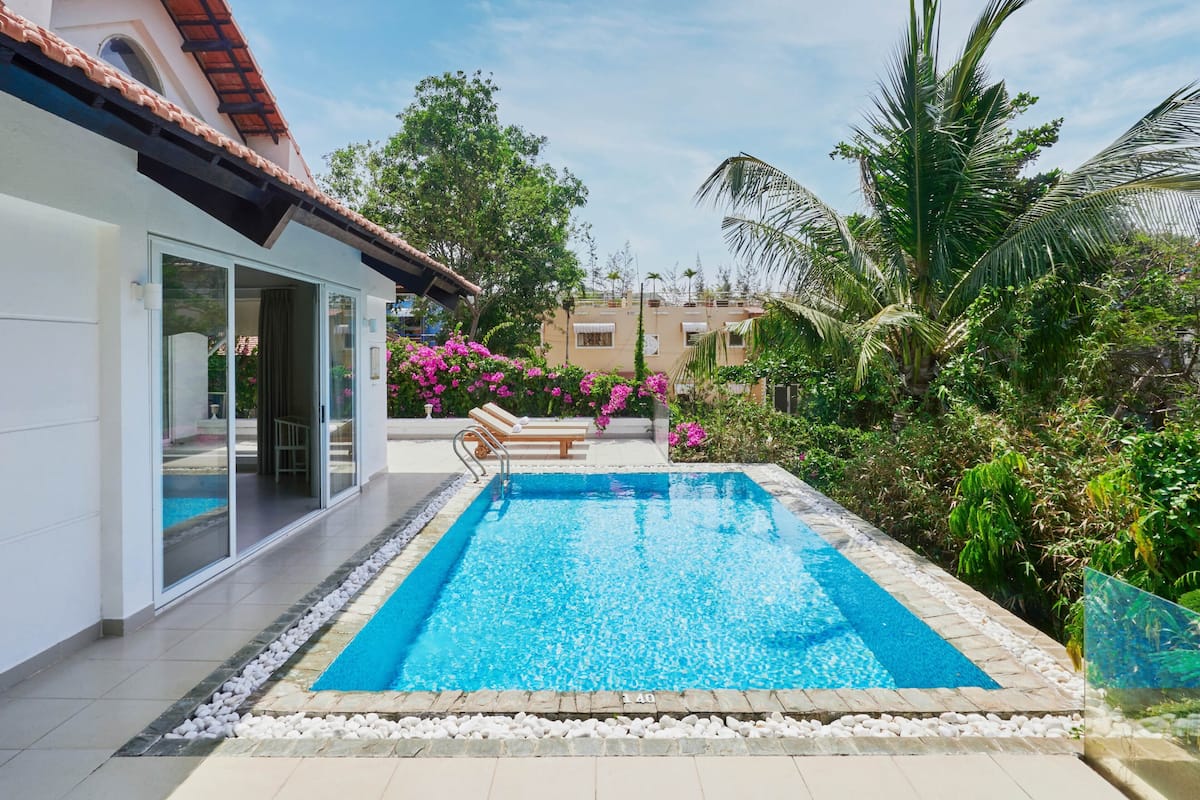 Une piscine dotée d’une terrasse carrelée, entourée de verdure et bordée d’un bâtiment dont le toit est également recouvert de tuiles.