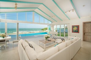A spacious living room with a large window overlooking a pool and ocean, a white sofa, a coffee table, and a piano. - Fleur de Lys Resort & Spa Long Hai (Ho Chi Minh Municipality)