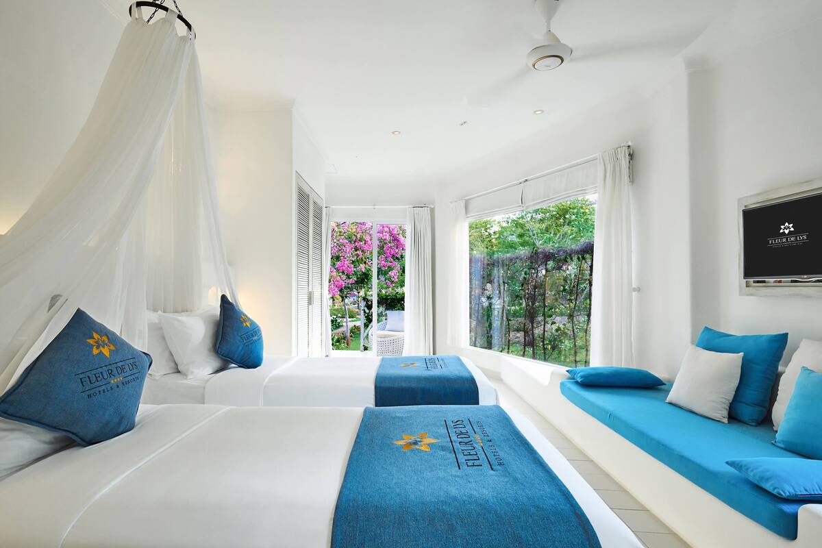 Une chambre d’hôtel avec deux lits, un lit à baldaquin, une vue sur la verdure et un ventilateur de plafond.