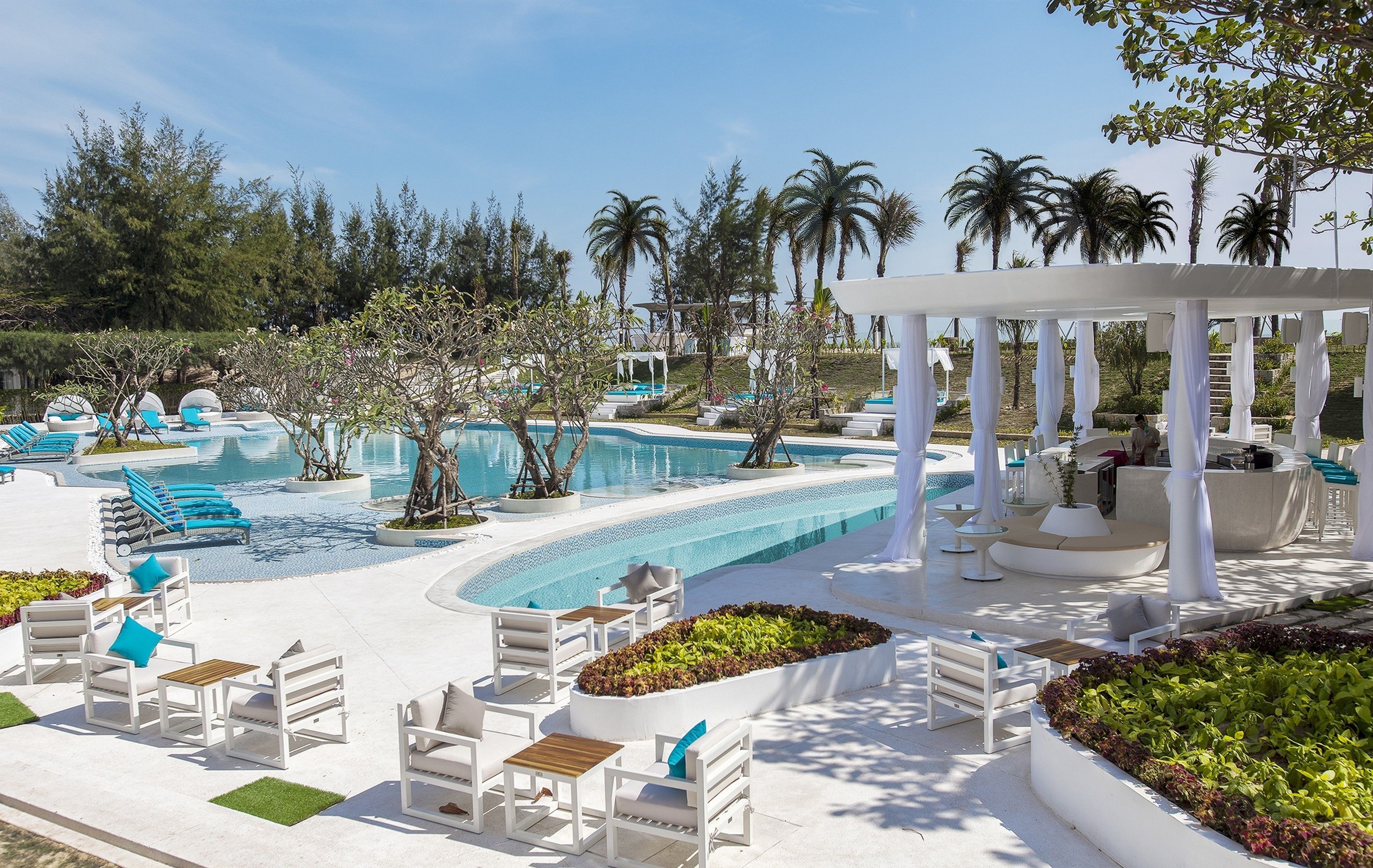 A resort pool area with lounge chairs, a covered seating area, and a landscaped garden.