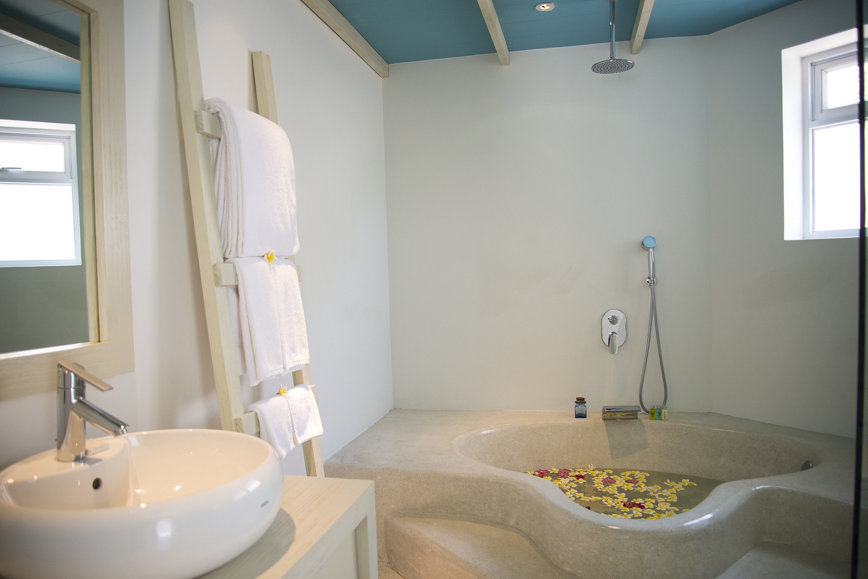 A bathroom with a sink, a bathtub filled with flower petals, and a showerhead.