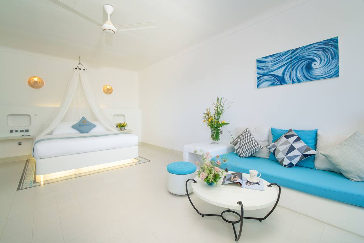 Une chambre d’hôtel moderne avec un lit, un canapé bleu, une table basse ronde et une œuvre d’art murale.