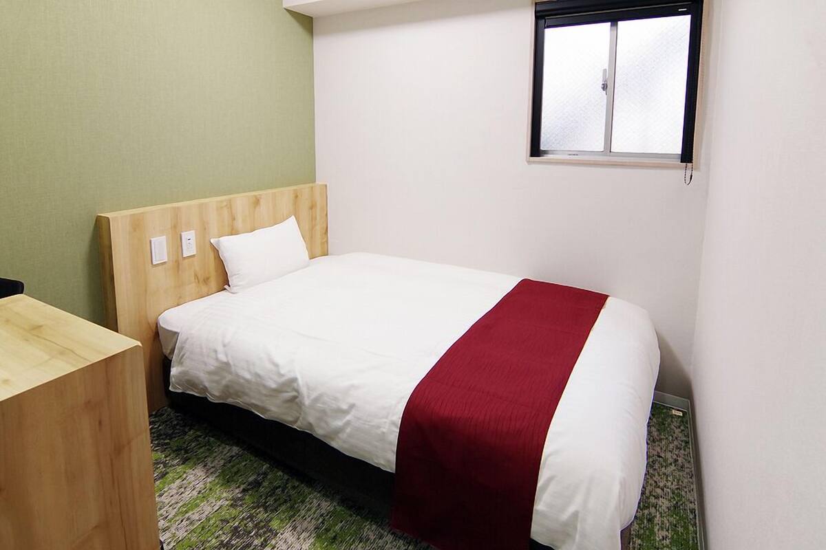 A single bed with a wooden headboard, white bedding, and a red accent.