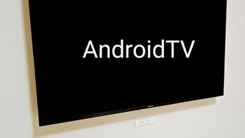 A flat-screen TV mounted on a wall with the text "AndroidTV" displayed on the screen.