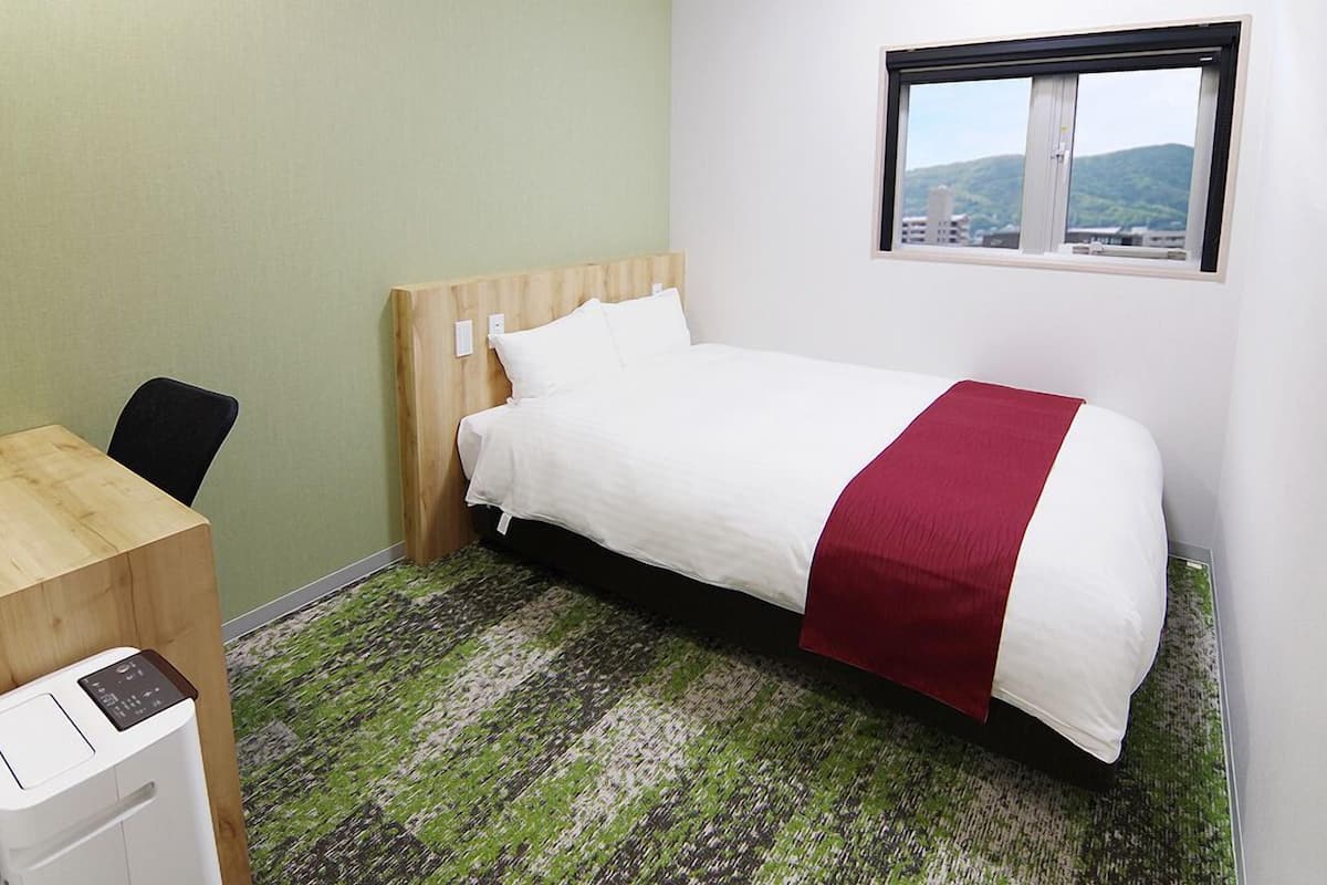 A hotel room with a bed, a desk, and a window.
