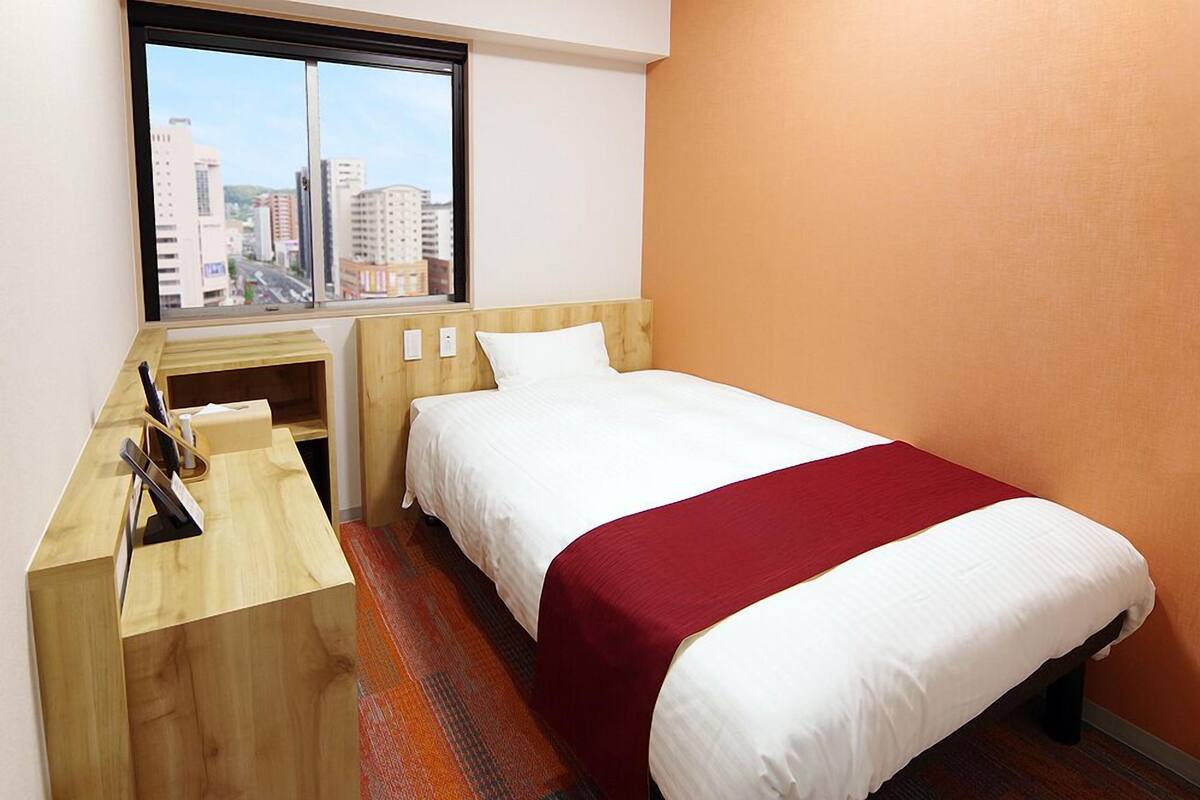A hotel room with a bed, a desk, and a window with a city view.