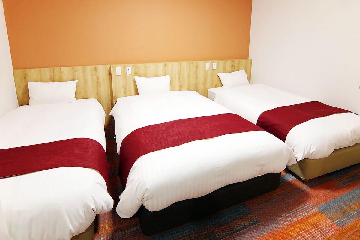 A hotel room with three beds arranged in a row, each with white bedding and red accents.