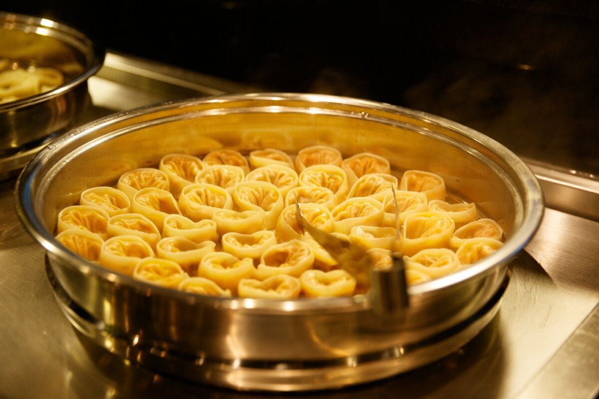 A stainless steel pot filled with neatly arranged pasta rolls.