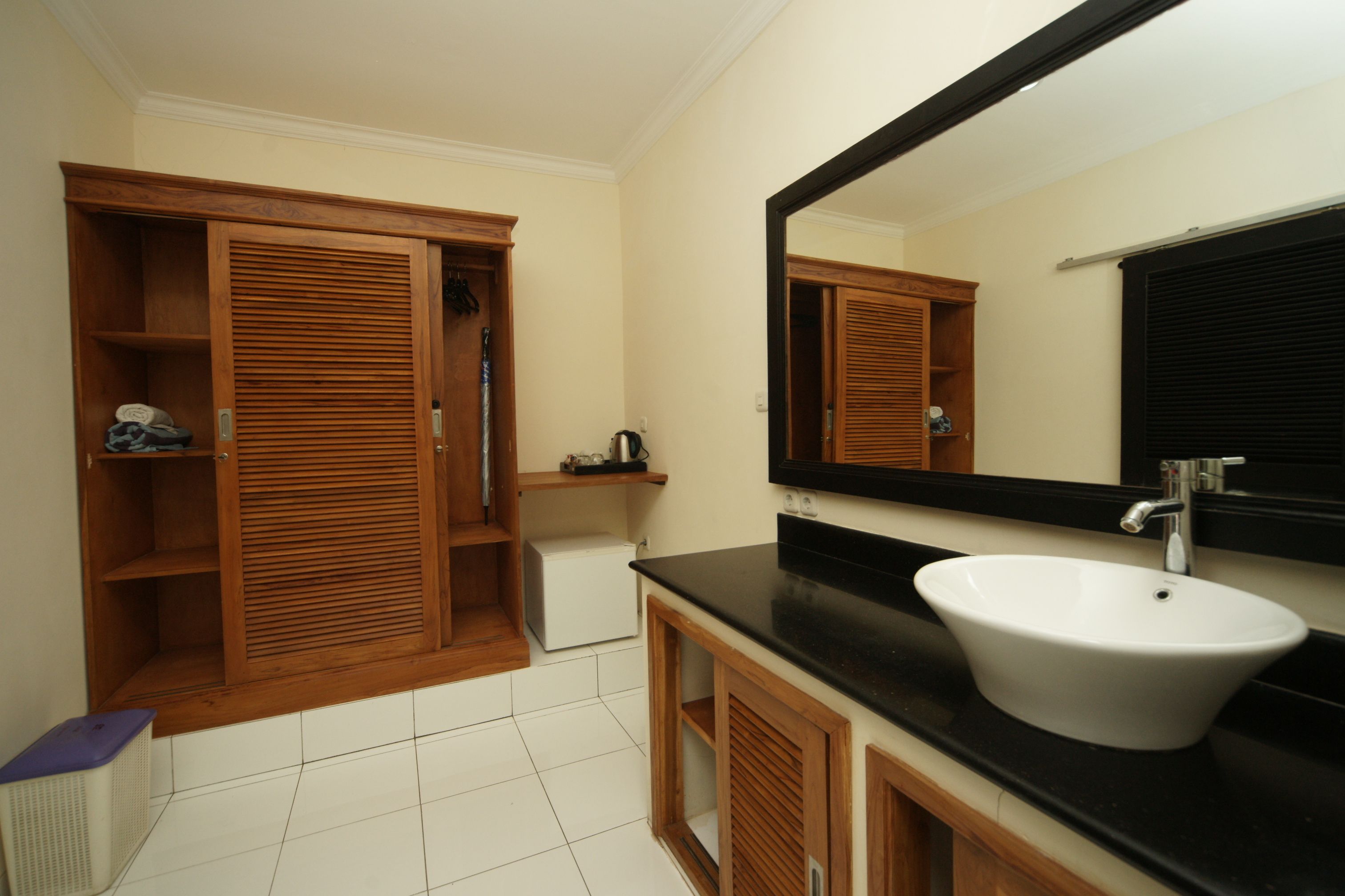 Un baño con tocador de madera, un lavamanos blanco y un espejo grande.