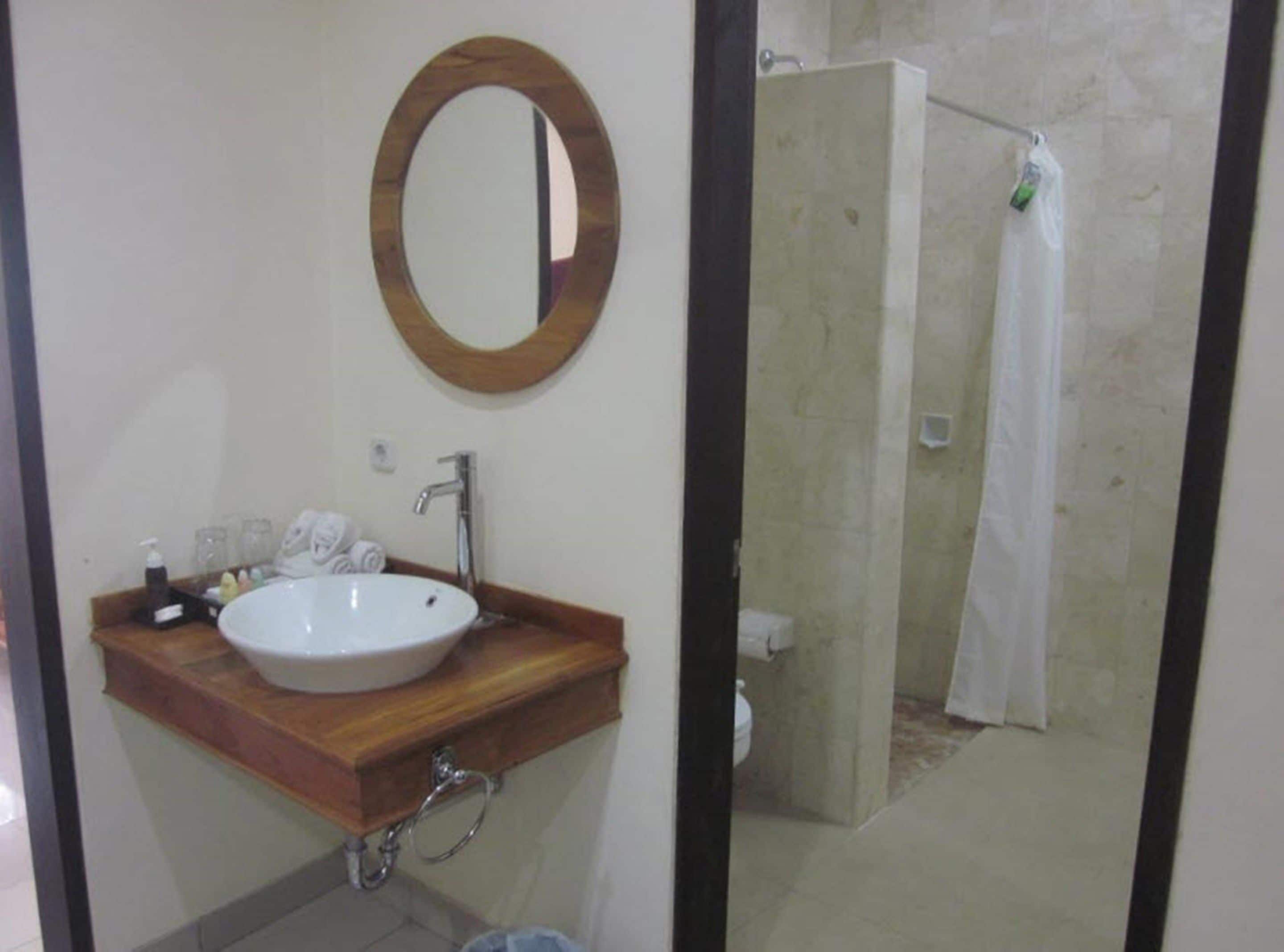 A bathroom with a wooden vanity, a white sink, a mirror, and a shower area.