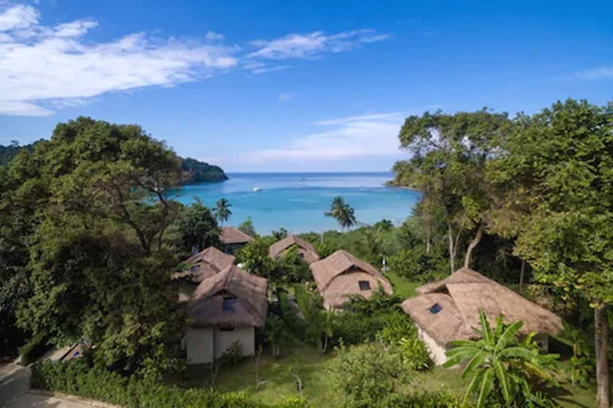 A coastal village with thatched-roof houses, lush greenery, and a clear view of the sea.