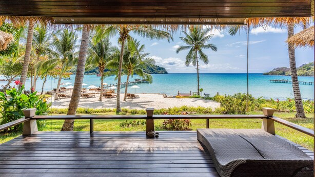 Eine Holzterrasse mit Blick auf einen Strand, Palmen und einen Steg.