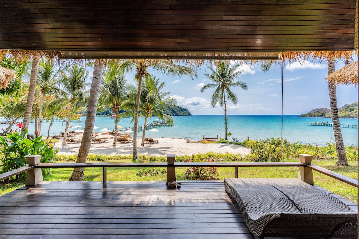 A wooden deck with a view of a beach, palm trees, and a pier.