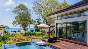 Ein moderner Poolbereich mit Holzterrasse, Liegestühlen und einer überdachten Glasveranda mit Blick auf eine malerische Meerlandschaft.