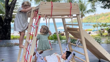 Relax on a wooden swing set with a hammock, overlooking a serene body of water and lush greenery.