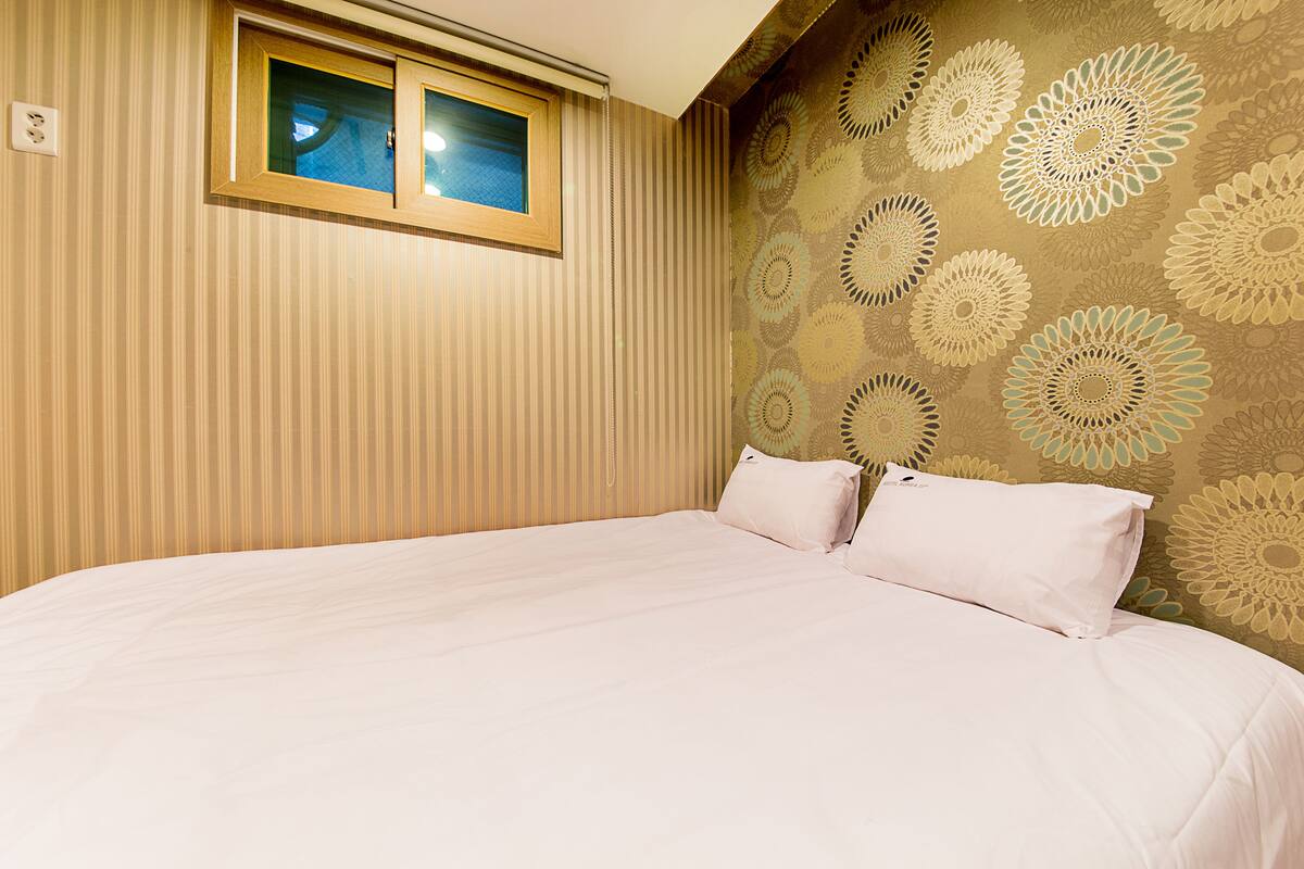 A bedroom with a large bed, two pillows, a window, and a wall with a floral pattern.