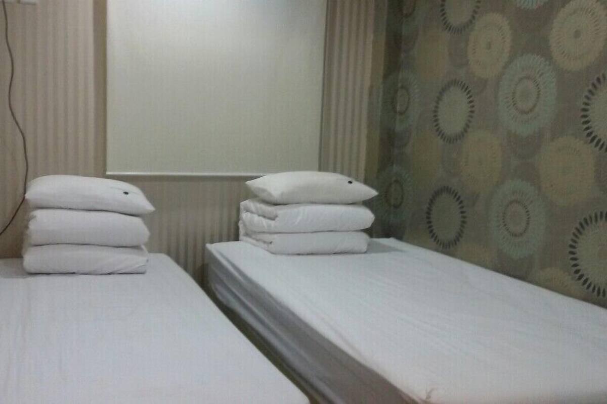 Two single beds with white linens and pillows, a radiator, and patterned curtains.