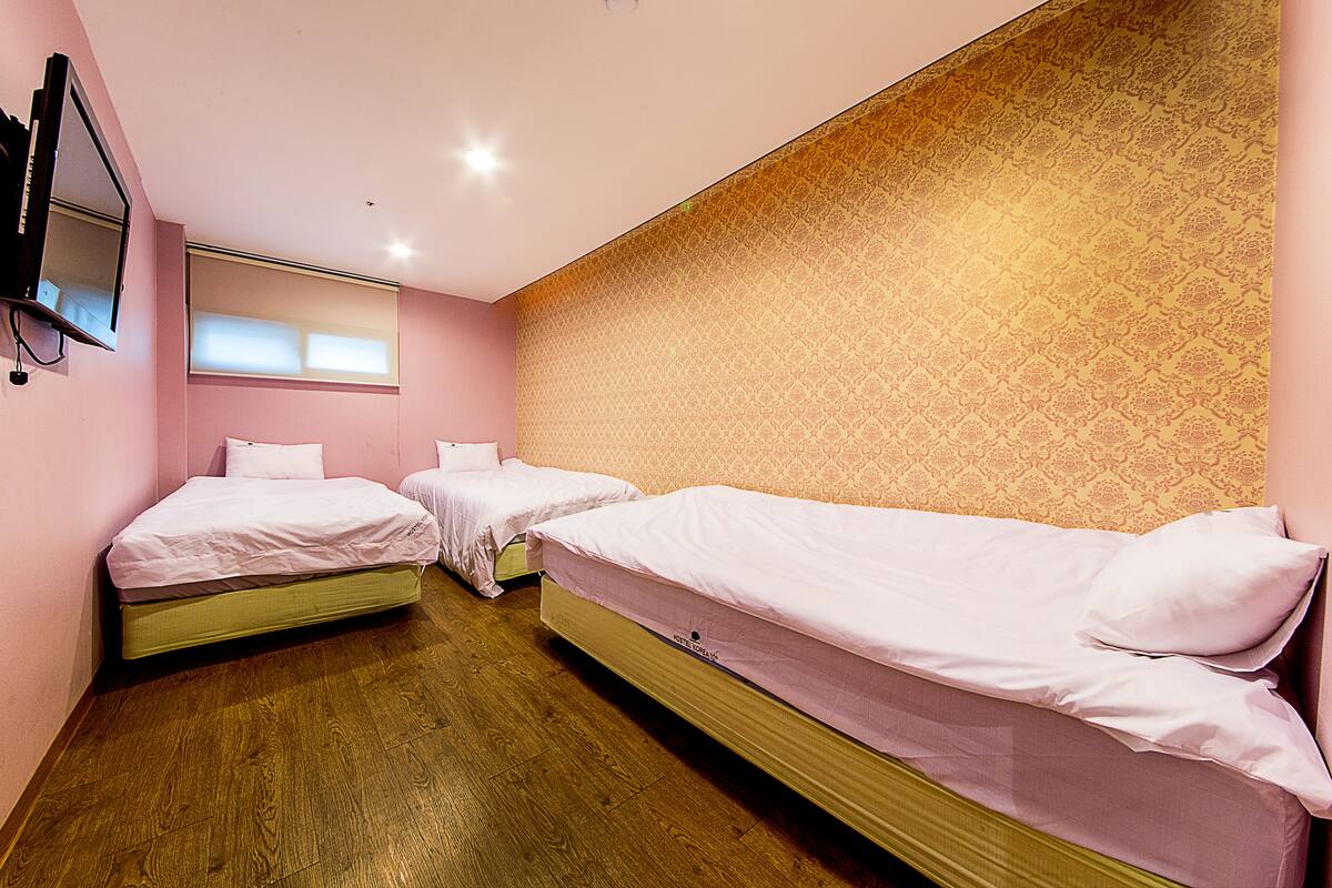 A hotel room with two single beds, a TV mounted on the wall, and a patterned wallpaper on the wall behind the beds.