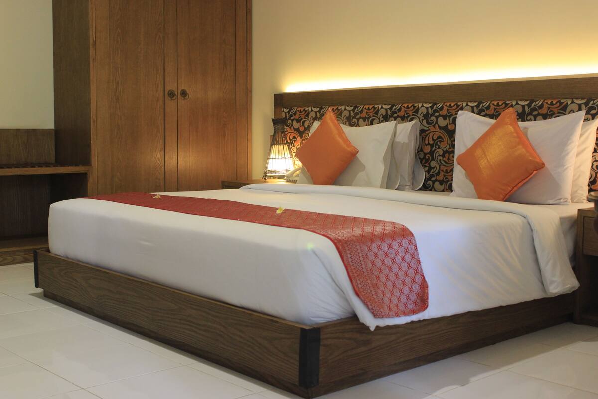 A neatly made bed with a wooden frame, a patterned headboard, and two orange pillows.