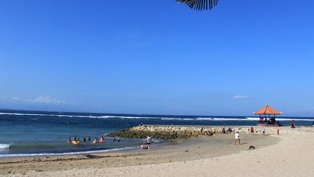 A beach with a gazebo, rocky shoreline, and people in the water. - Jambu Inn Sanur Beach (Denpasar)
