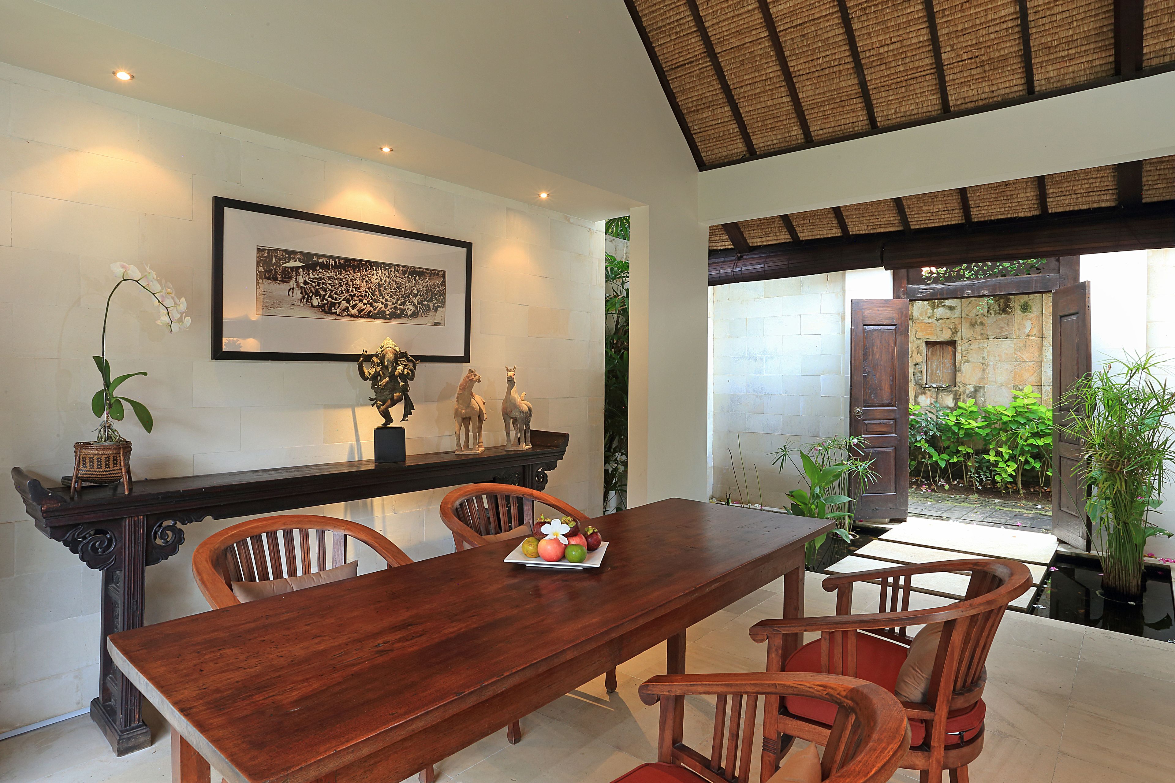 Un coin repas avec une table et des chaises en bois, un tableau encadré au mur et une petite plante en pot posée sur la table.