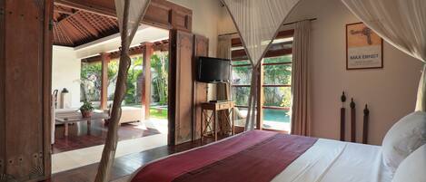 A bedroom with a large bed, wooden furniture, a television, and a view of the outdoors.